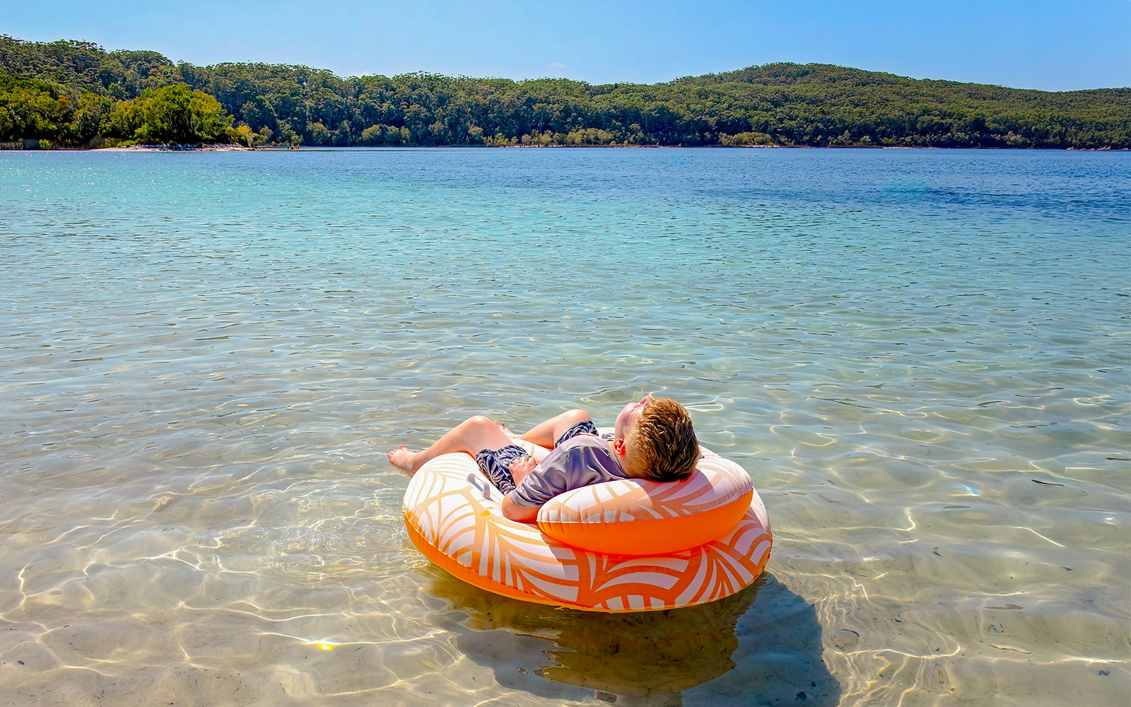 Boy floating on an inflatable ring in Lake McKenzie, Fraser Island, K'gari.