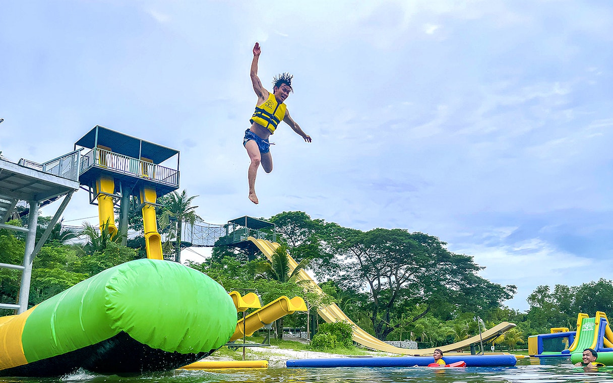 Person jumping from platform at ESCAPE Ipoh Theme Park with water slides and inflatable structures.
