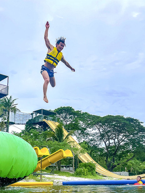 Person jumping from platform at ESCAPE Ipoh Theme Park with water slides and inflatable structures.