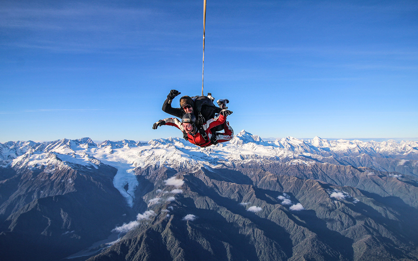 Skydivers over Franz Josef Glacier with snow-capped mountains in New Zealand.