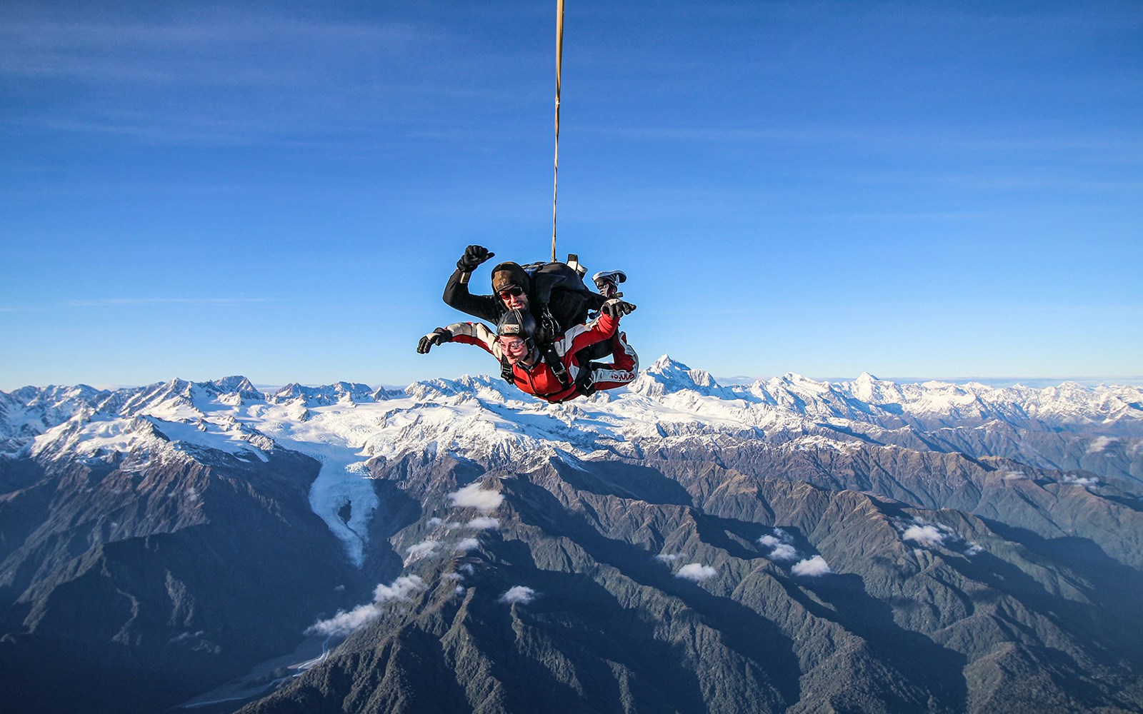 Skydivers over Franz Josef Glacier with snow-capped mountains in New Zealand.
