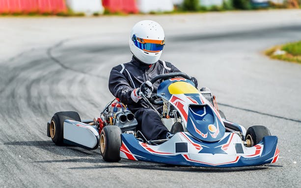 Gokart racing on an outdoor circuit with a driver in full gear.