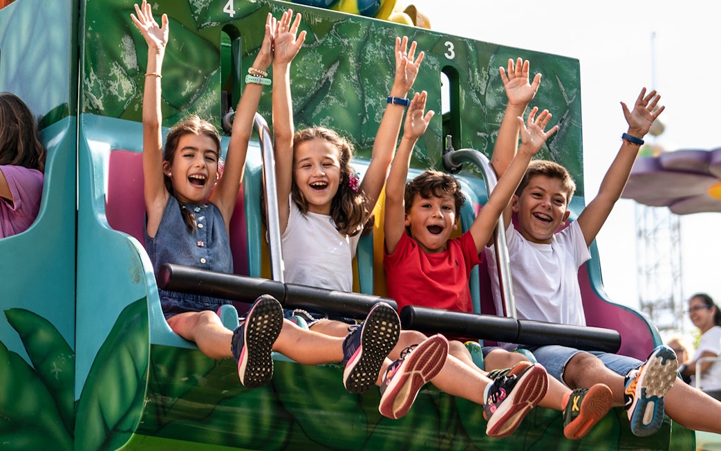 Children enjoying a ride at Isla Mágica, Seville, with arms raised in excitement.