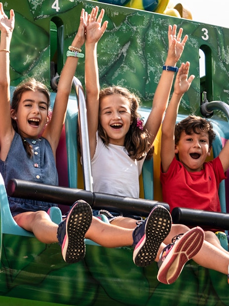 Children enjoying a ride at Isla Mágica, Seville, with arms raised in excitement.