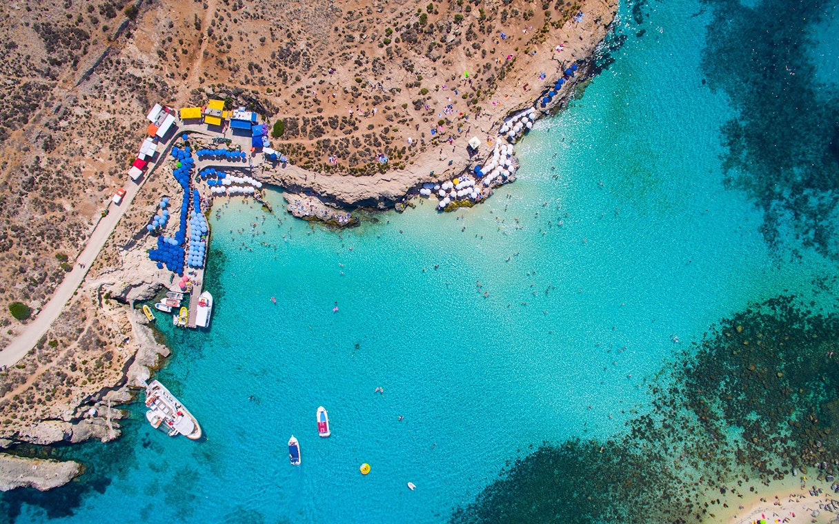 Aerial view of Blue Lagoon, Malta with boats and sunbathers along the rocky coastline.