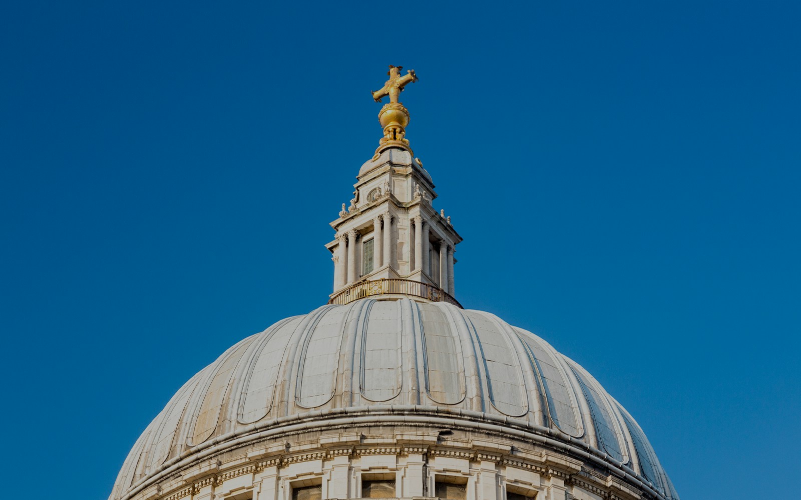 Dome and cross of St. Paul's Cathedral, London against blue sky.