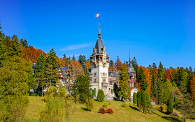 Peles Castle with ornate architecture surrounded by autumn trees in Sinaia, Romania.