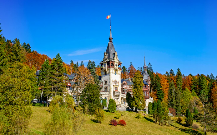 Peles Castle with ornate architecture surrounded by autumn trees in Sinaia, Romania.