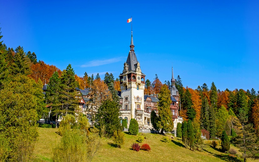 Peles Castle with ornate architecture surrounded by autumn trees in Sinaia, Romania.