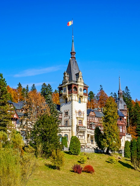 Peles Castle with ornate architecture surrounded by autumn trees in Sinaia, Romania.