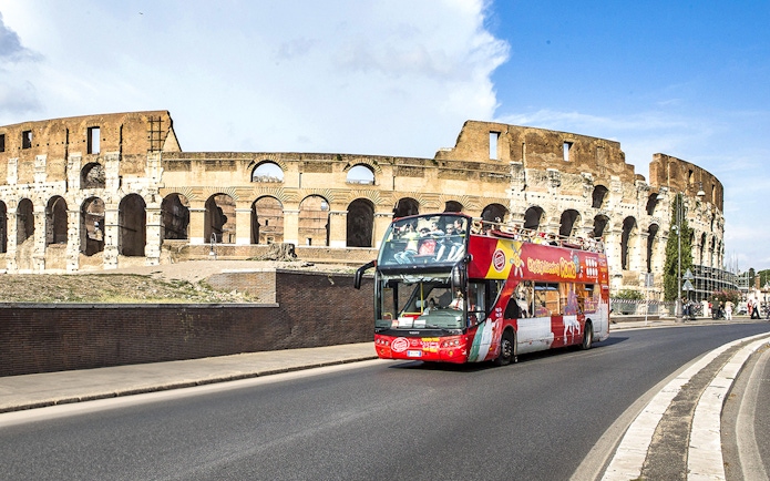 Open-top tour bus passing the Colosseum in Rome.