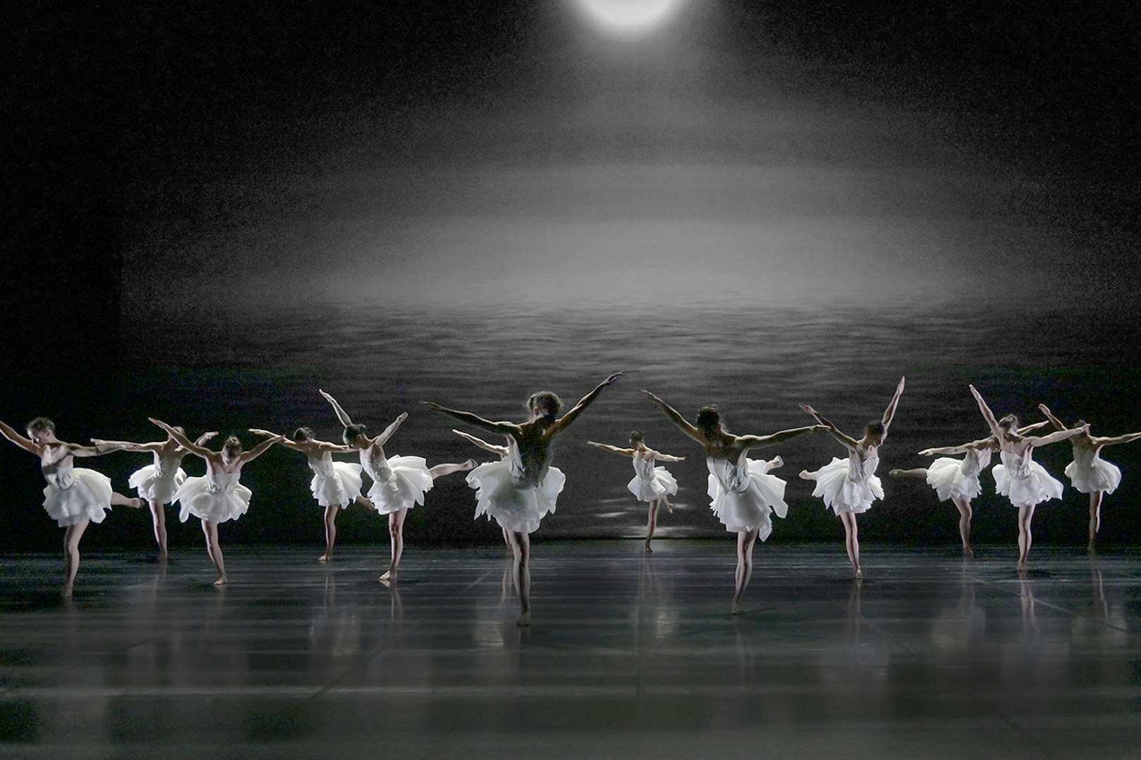 Ballet dancers performing Swan Lake by Preljocaj on a dimly lit stage.
