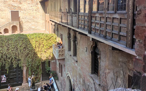 Visitors at Juliet's balcony in Verona, Italy, with ivy-covered walls and courtyard below.