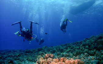 Divers ascending towards a boat over coral reefs in Maui.
