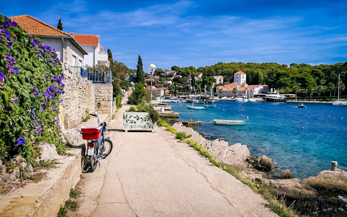 Pathway along Maslinica harbor with boats and stone houses, part of Trogir's Blue Lagoon tour.