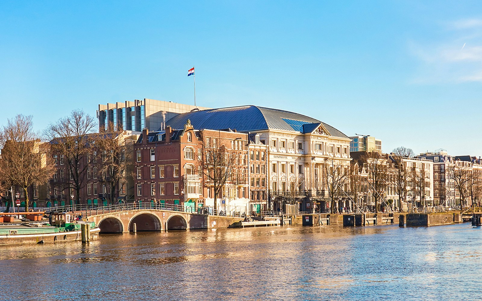 Carré Theater overlooking Amsterdam's Amstel River with boats passing by.