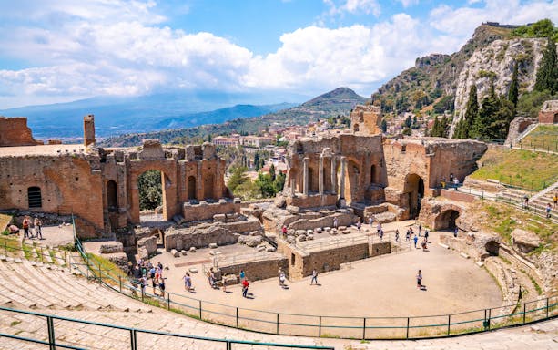 Taormina Ancient Theatre with scenic hillside and visitors exploring ruins.