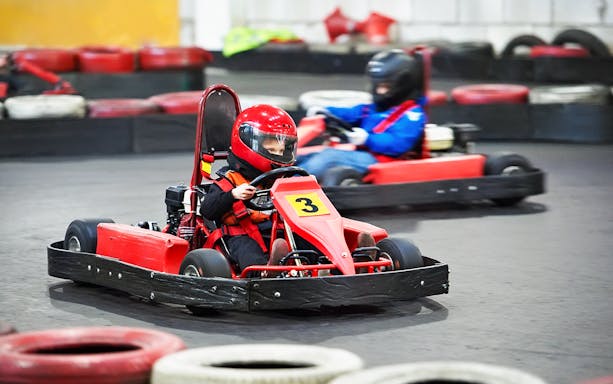 Child driving a red go-kart on an indoor track.