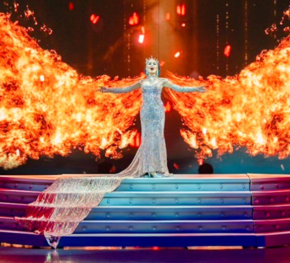 Performer in sparkling gown on stage with fiery backdrop at Colosseum Cabaret Show Pattaya.