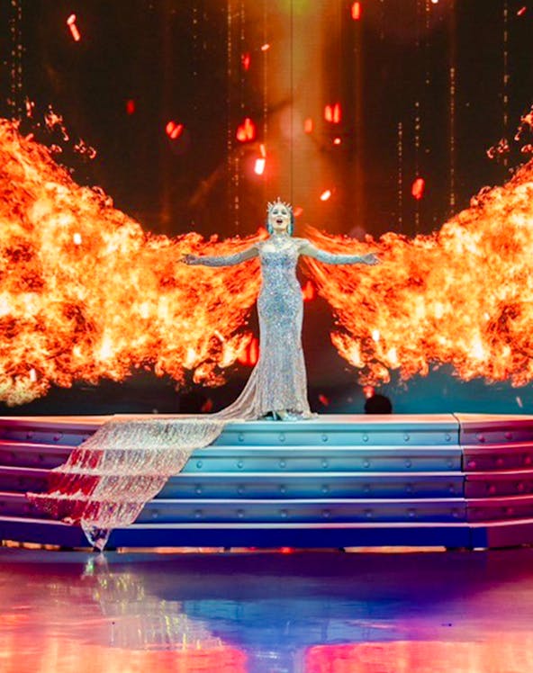 Performer in sparkling gown on stage with fiery backdrop at Colosseum Cabaret Show Pattaya.