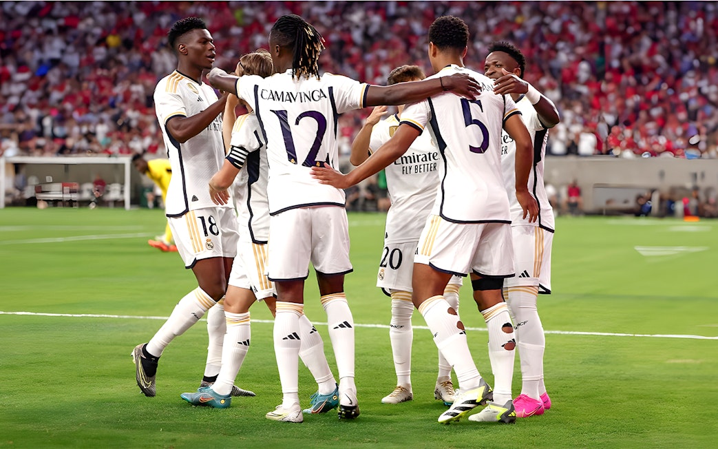 Soccer players in white jerseys huddling on a field during a match.