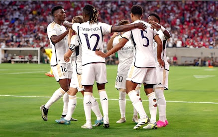 Soccer players in white jerseys huddling on a field during a match.