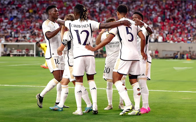 Soccer players in white jerseys huddling on a field during a match.