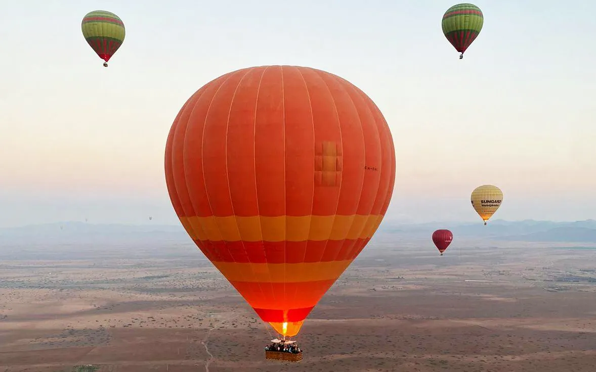 Hot air balloons floating over Marrakesh desert at sunrise.
