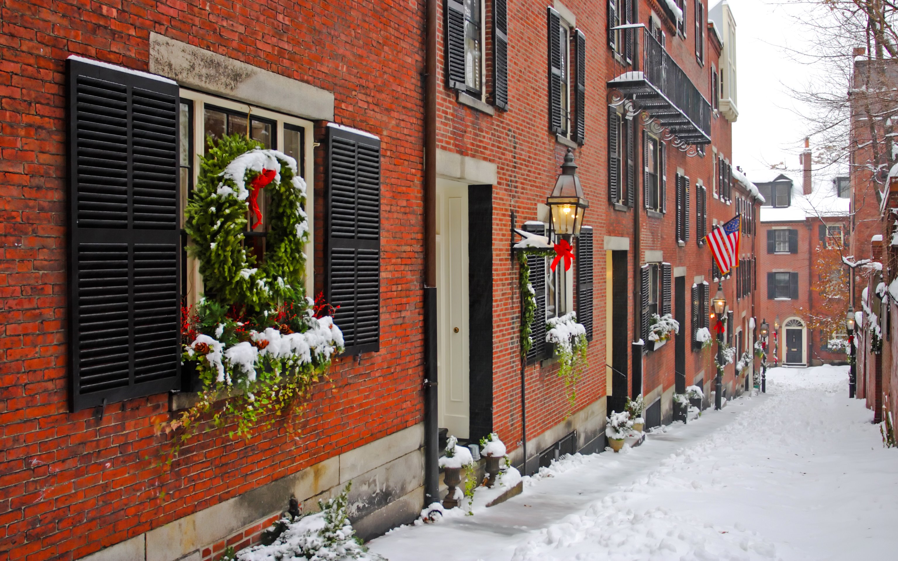 Snow-covered street with brick buildings and holiday wreaths in Beacon Hill, Boston.