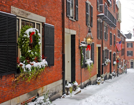 Snow-covered street with brick buildings and holiday wreaths in Beacon Hill, Boston.