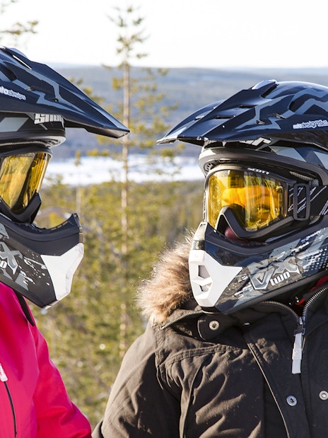 Two people in winter gear with helmets, preparing for a snowmobile sprint in Rovaniemi.