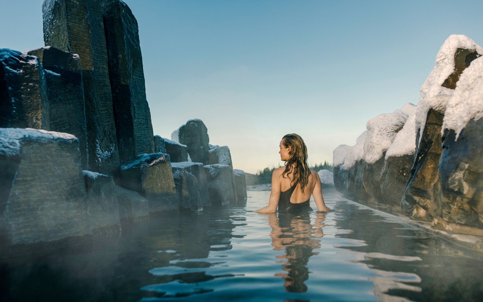 Person relaxing in a secluded grotto at Laugarás Lagoon, surrounded by snow-covered rocks.