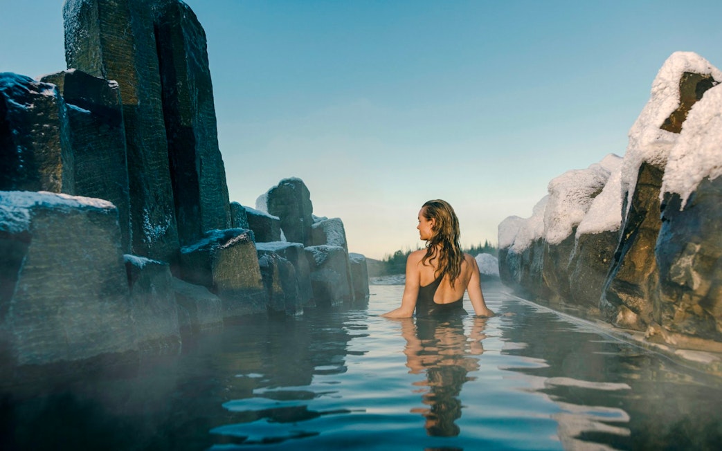 Person relaxing in a secluded grotto at Laugarás Lagoon, surrounded by snow-covered rocks.