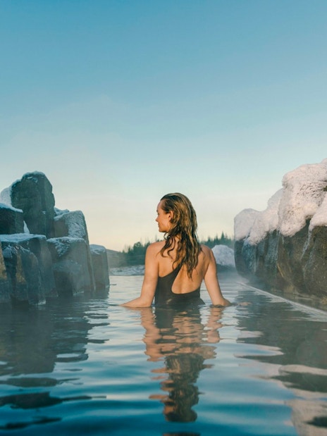 Person relaxing in a secluded grotto at Laugarás Lagoon, surrounded by snow-covered rocks.