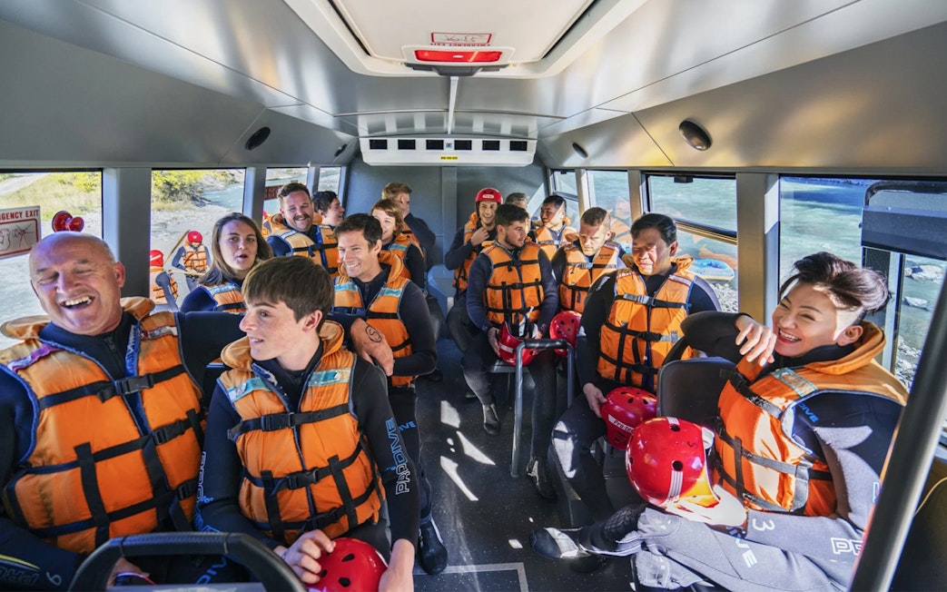 Group of people in life jackets on a bus for Shotover River rafting in Queenstown.