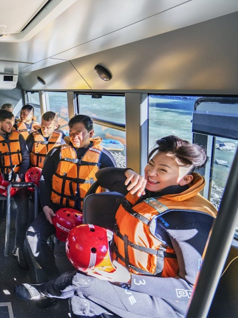 Group of people in life jackets on a bus for Shotover River rafting in Queenstown.