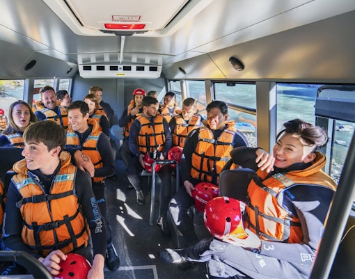 Group of people in life jackets on a bus for Shotover River rafting in Queenstown.