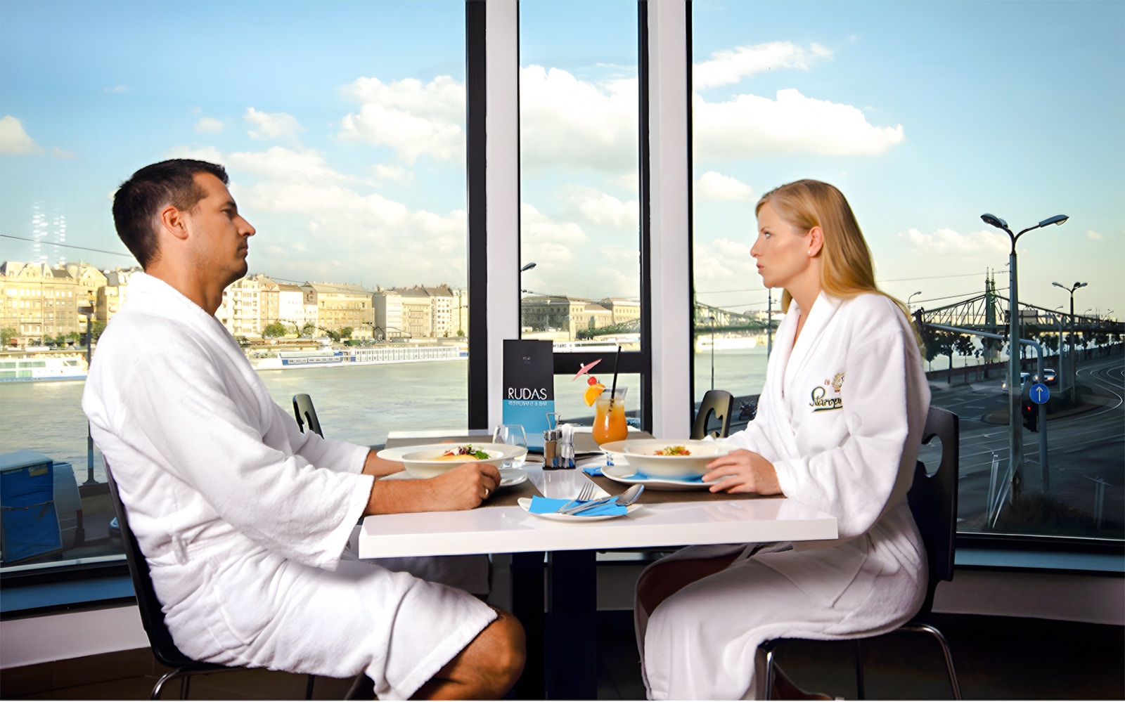 Couple in robes dining at Rudas Bath restaurant with indoor seating in Budapest.