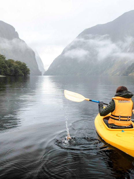 Person kayaking on Doubtful Sound with misty mountains in the background.