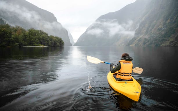 Person kayaking on Doubtful Sound with misty mountains in the background.