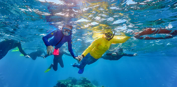 Snorkeling family exploring coral reef on Cairns to Green Island cruise.