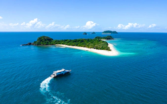 Boat approaching Frankland Islands, Queensland, with lush greenery and sandy beaches.