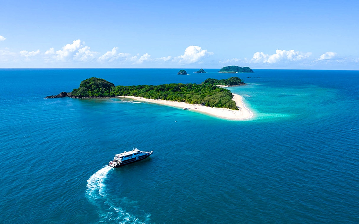 Boat approaching Frankland Islands, Queensland, with lush greenery and sandy beaches.
