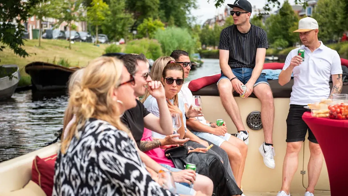 Group enjoying Harlem canal cruise on open boat with drinks and snacks.