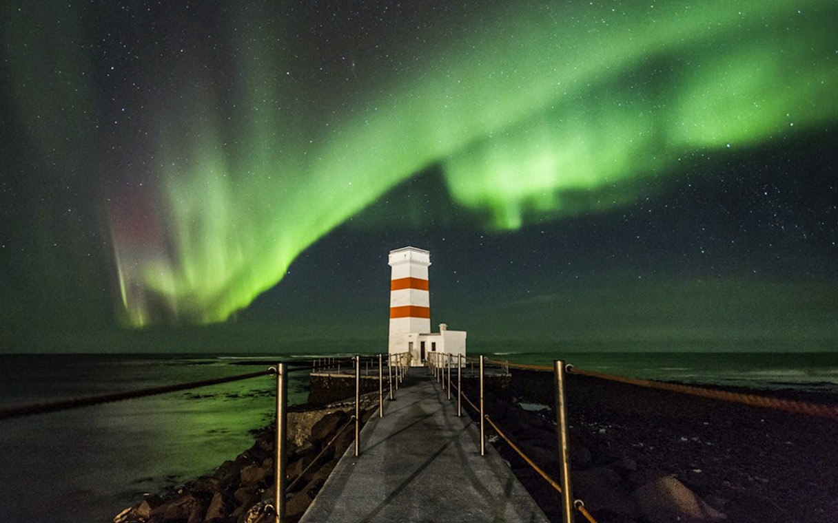 Northern Lights over a lighthouse on an off-road tour path, Iceland.