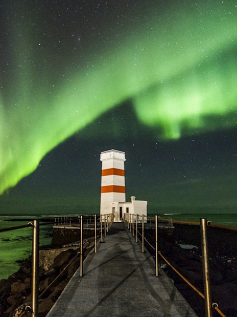 Northern Lights over a lighthouse on an off-road tour path, Iceland.