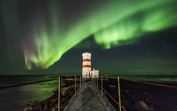 Northern Lights over a lighthouse on an off-road tour path, Iceland.