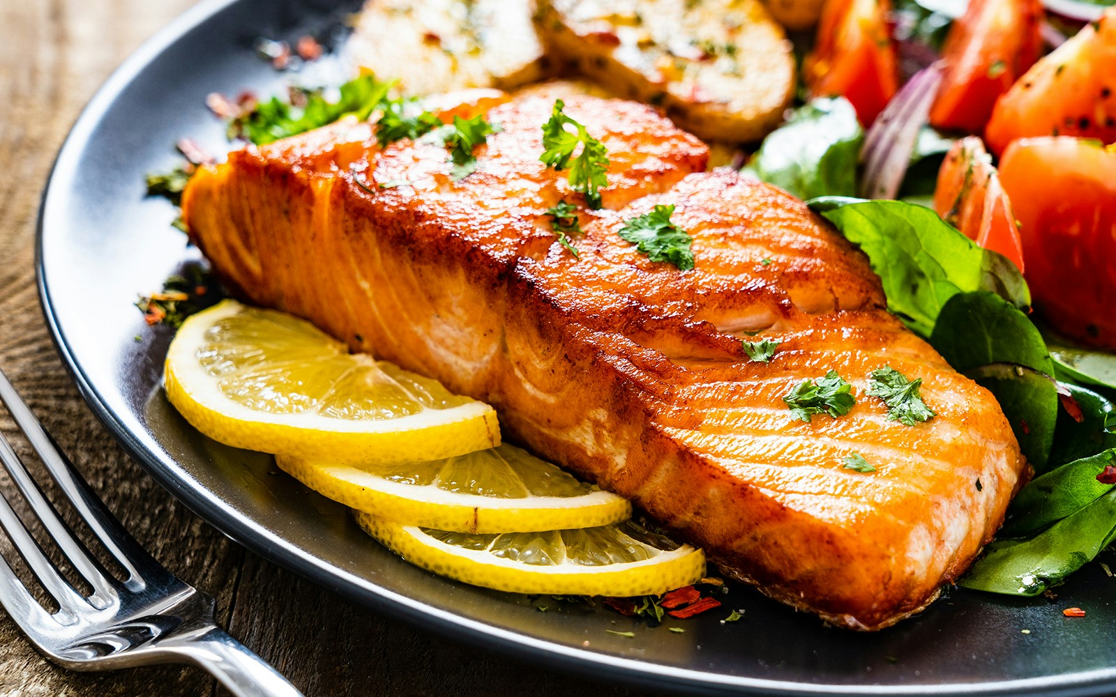 Fried salmon steak with lemon slices and salad on a plate for lunch.