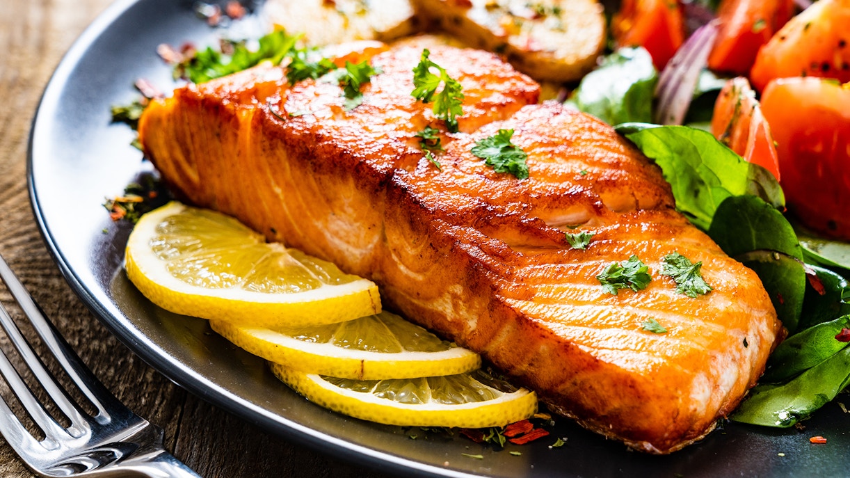 Fried salmon steak with lemon slices and salad on a plate for lunch.