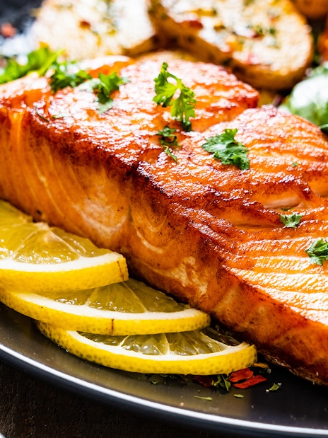 Fried salmon steak with lemon slices and salad on a plate for lunch.